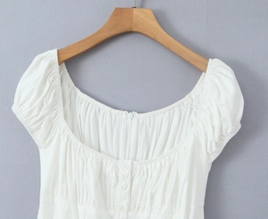 Détail du col carré et des manches bouffantes sur robe blanche avec boutons décoratifs