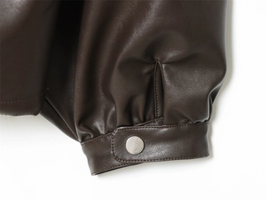 Close-up of dark brown PU leather jacket cuff with silver metal button and stitching details