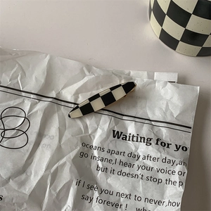 Retro black and white checkerboard hair clip displayed on a minimalist lyric paper background