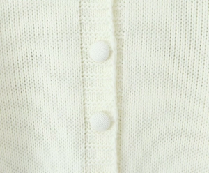 Macro detail of the fine-knit beige cardigan fabric and matching cloth-covered buttons