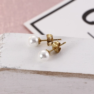Detailed close-up of classic pearl stud earrings in gold titanium steel on white wood