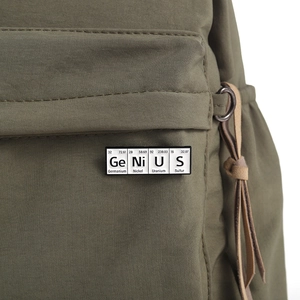 Close-up of GeNiUS periodic table enamel pin on a green canvas backpack texture