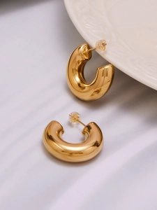 Polished hollow C-shaped gold earrings with silicone backs on white silk fabric