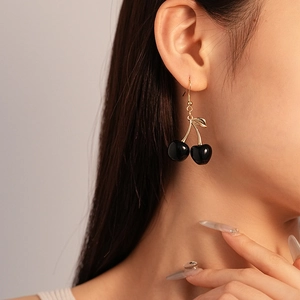 Detail of dark resin cherry drop earrings with gold hooks worn by a model in soft light