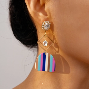 Close-up of geometric dangle earrings with crystal studs and striped acrylic pendants