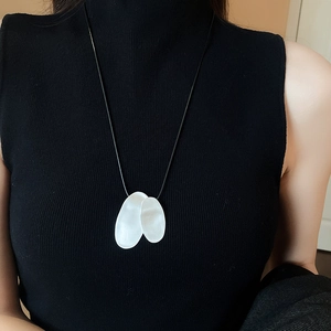 Detailed view of silver irregular oval pendants on black cord necklace worn on black sweater