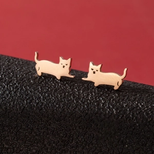 Macro shot of minimalist gold cat-shaped stainless steel earrings on a textured background