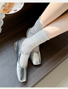 Dettaglio di scarpe Mary Jane argento con calze in maglia grigia su scale di legno