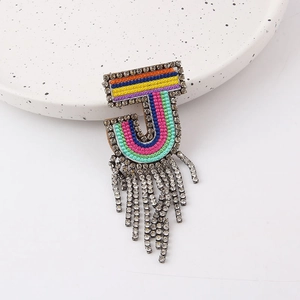 Macro shot of colorful letter J brooch with sparkling rhinestone fringe on ceramic