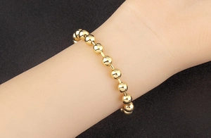 Detailed view of an 18k gold plated bead bracelet on wrist with high metallic luster