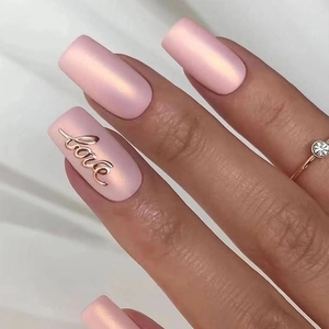 Gros plan d'ongles mats roses avec lettrage LOVE doré en relief et finition soignée