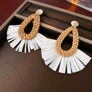 Detailed macro view of woven brown water drop studs and white raffia tassel earrings