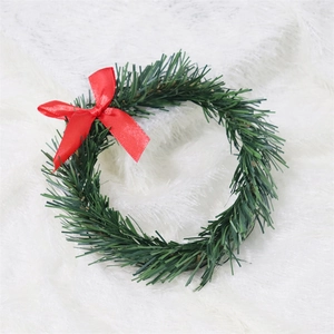 Close-up of small green PVC pine wreath with a red bow on white plush fabric texture