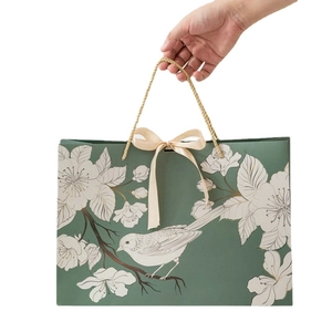 Green paper gift bag with white floral bird pattern and beige silk ribbon bow handle