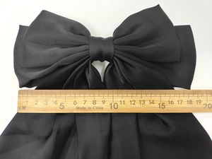 Detail showing a 20cm oversized black satin bow hair clip measured with a wooden ruler