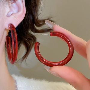 Detail of a red resin C-shaped hoop earring worn by a model in a warm-toned setting
