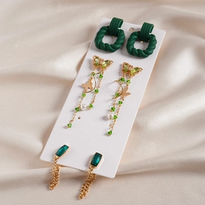 Detailed set of three green acrylic butterfly and gold tassel earrings on silk fabric
