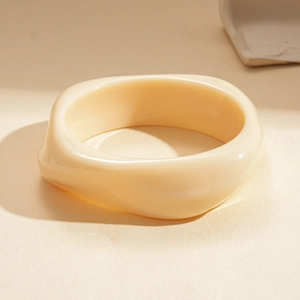 Vue macro d'un bracelet large en acrylique crème avec une géométrie ondulée irrégulière