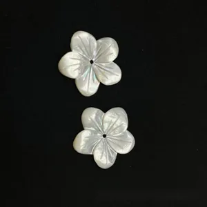 Macro shot of two white shell flower charms with five petals and center holes for DIY