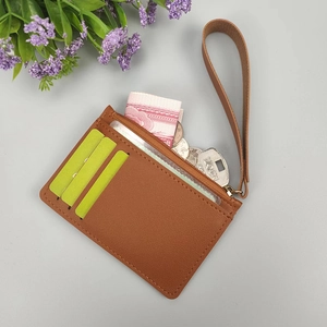 Dettaglio porta carte sottile in pelle marrone con tasca zip e cinturino da polso
