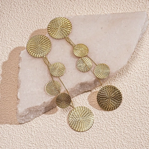 Detail of long gold tassel earrings featuring textured metal circles on a stone base