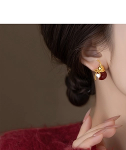 Detailed view of gourd-shaped gold earrings with red beads and zircon on a model