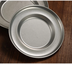 Close-up of stacked matte stainless steel soup plates on a dark wooden background