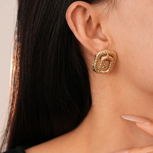 Close-up of golden irregular spiral earrings featuring a textured lava metal finish