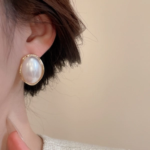 Detailed view of elegant oval pearl earrings with vintage gold wavy metal edges on ear