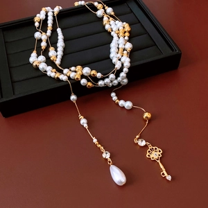 Close-up of multilayer pearl necklace with gold key and teardrop pearl pendant detail