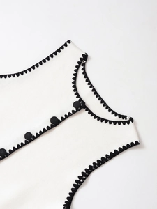 Detailansicht der weißen Strickweste mit schwarzem Wellensaum und passenden Knöpfen