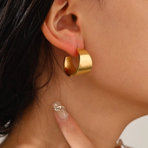Macro view of gold plated chunky C-shaped hoop earrings worn on ear with polished finish