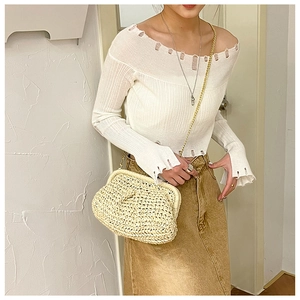 Detail of straw woven crossbody bag featuring a golden chain strap on a white open shoulder top