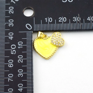 Detailed view of a gold-plated heart pendant with zircon inlay next to a ruler for size