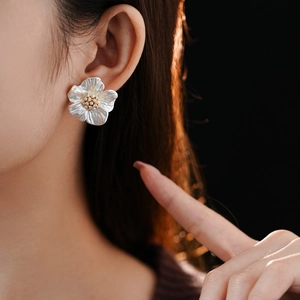 Close-up of elegant white flower stud earrings with pearl-like texture and gold core on ear