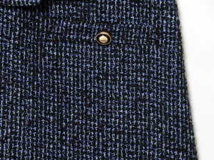 Detailopname van blauwe en zwarte tweed stof met een decoratieve gouden knoop erop
