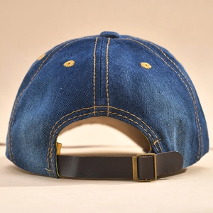 Detail of blue denim baseball cap with brown leather strap and brass metal buckle closure