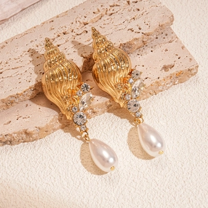 Detail of conch shell earrings with sparkling rhinestones and drop pearl on stone