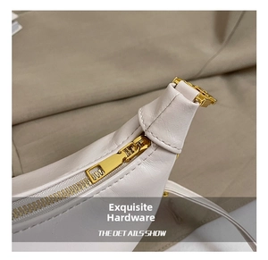 Close-up of polished gold-tone metal zipper and hardware on white leather handbag