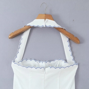 White halter top with blue scalloped embroidery hanging on a wooden hanger
