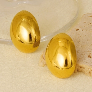 Macro shot of polished gold water drop earrings on textured stone and glass background