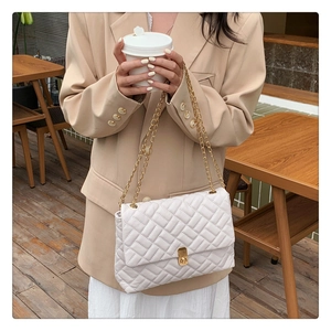 Close-up of white quilted shoulder bag with gold chain strap and metal swivel lock detail