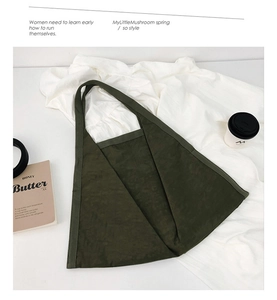 Flat lay of a dark green suede tote bag with minimalist triangle handle on white fabric