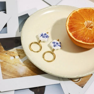 Dettaglio di orecchini in ceramica con motivi floreali blu e cerchi in acciaio dorato 18K