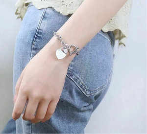 Détail d'un bracelet coeur en argent avec fermoir OT porté au poignet d'un mannequin