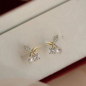 Elegant cherry pearl earrings in gold and diamonds resting on a beige jewelry case