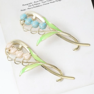 Detailed macro view of lily of the valley hair clips with green leaves and pink enamel finish