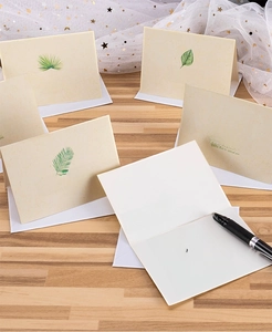 Close-up of beige message cards with green leaf patterns and white envelopes on wood