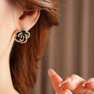 Close-up of elegant black rose stud earrings with gold rim and shimmering rhinestones