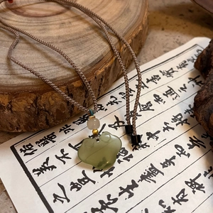 Detail of green jade Ruyi lock pendant with brown woven cord on wood and calligraphy